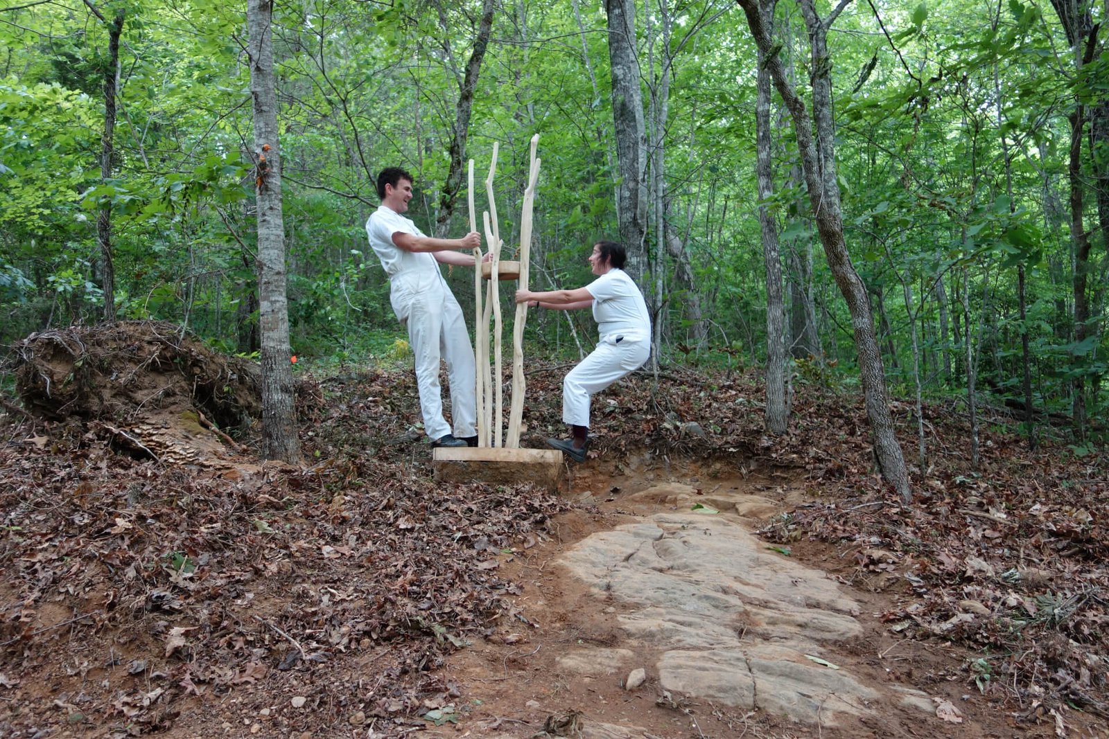 Two people rocking a large concrete pestle with oak sapling handles