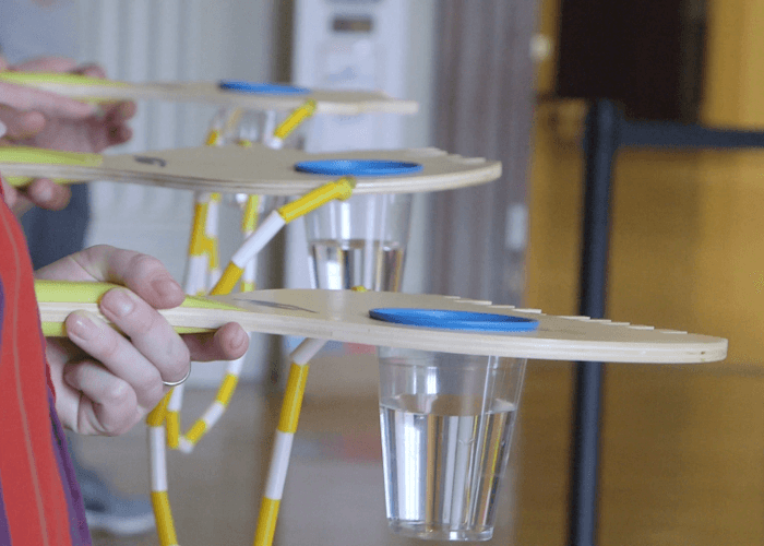 4 very large ping pong like paddles joined by lengths of white and yellow jump rope cut into the shape of Philadelphia neighborhoods with cups of water sunk into the surface of each paddle