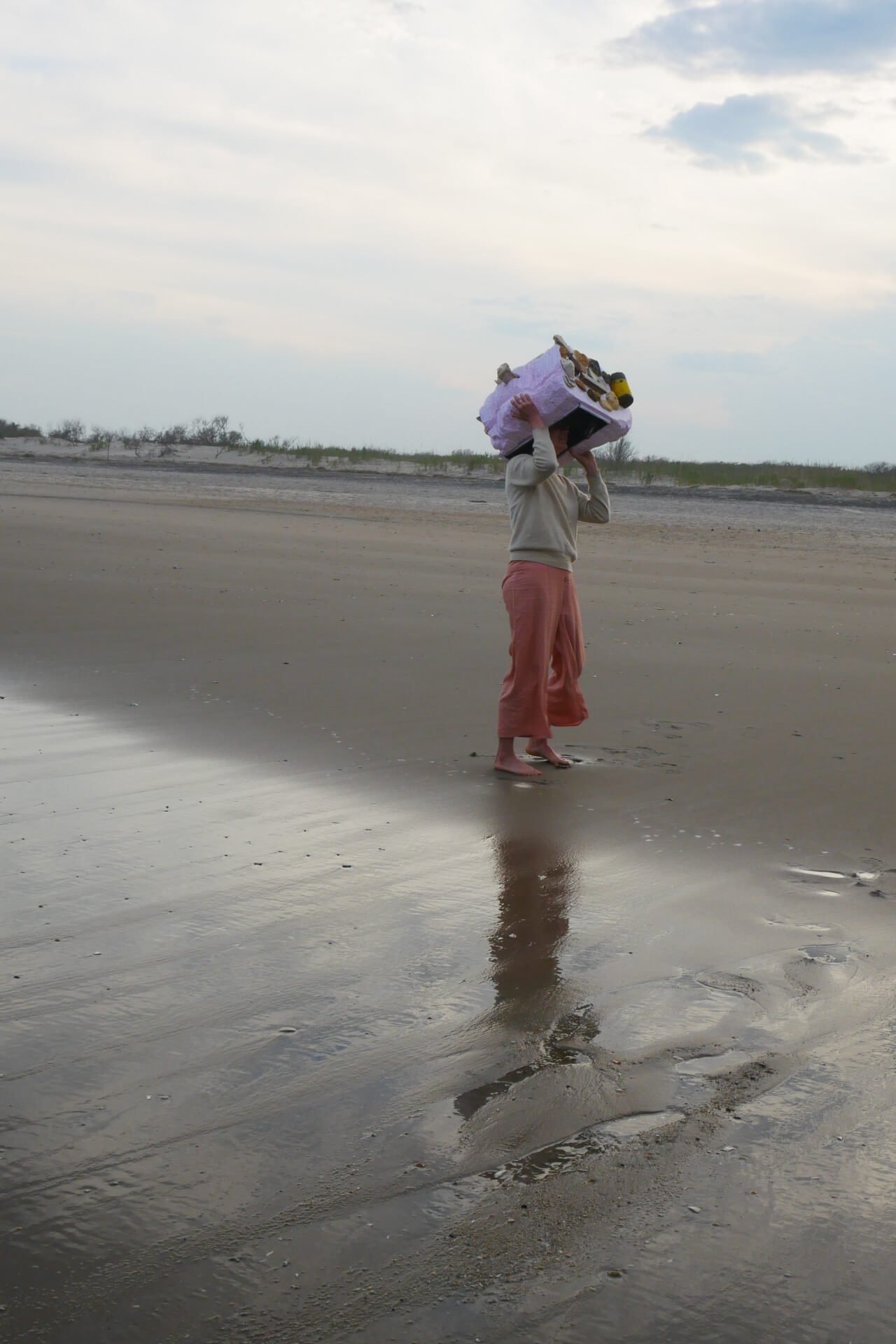 A person standing on the beach wearing a Plastic Dance helmet dancing.
